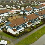 Drönarbild på vita och blåa radhus med uterum och små trädgårdar i ett bostadsområde