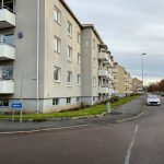 Beige lägenhetshus med fönster och balkonger längs en väg med bilar