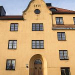 Framsidan på gult lägenhetshus med svarta fönster