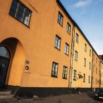 Orange lägenhetshus med svarta fönster vid en väg med bilar